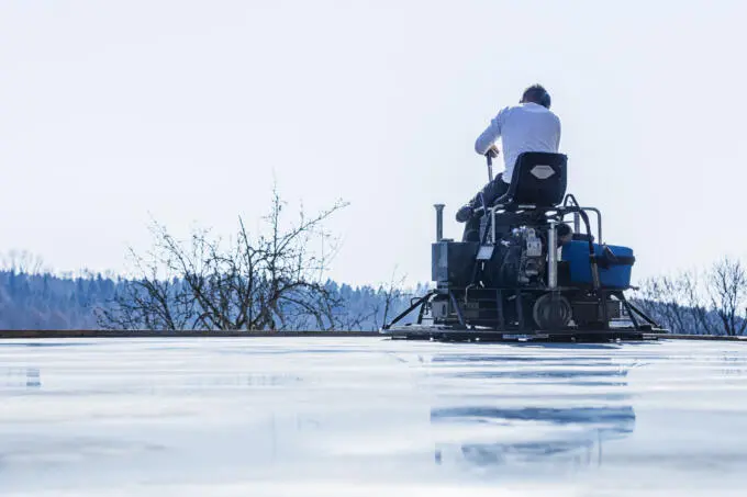 Rückansicht eines Arbeiters auf einem Aufsitz-Flügelglätter beim Glätten einer nassen Betonfläche im Freien