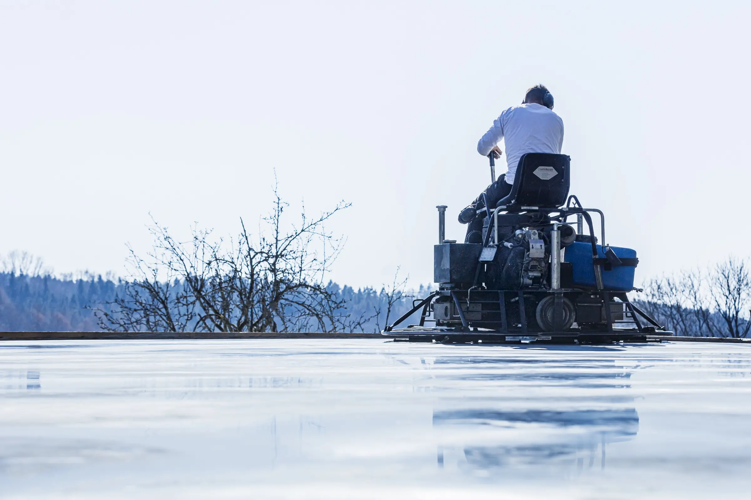 Rückansicht eines Arbeiters auf einem Aufsitz-Flügelglätter beim Glätten einer nassen Betonfläche im Freien