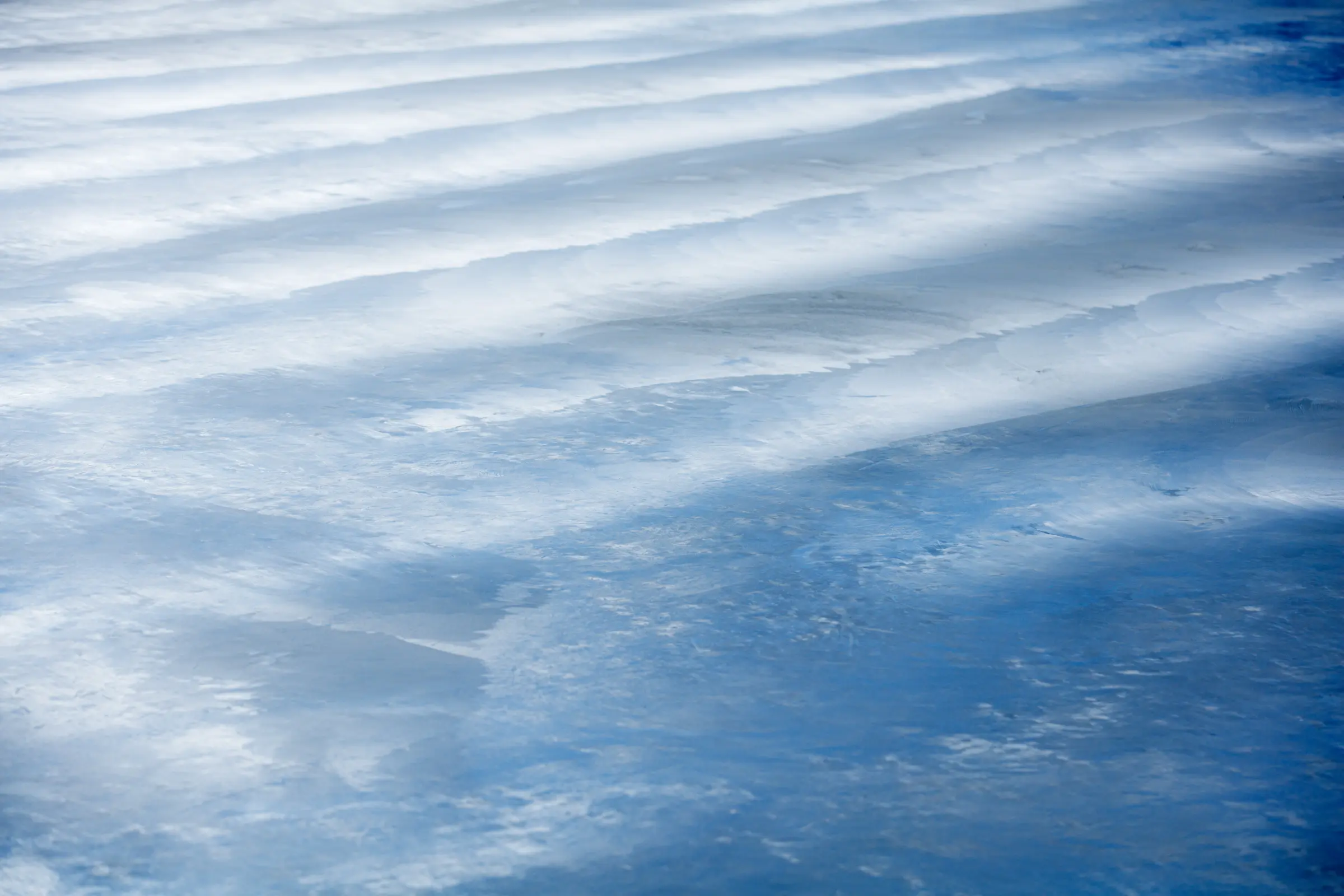 Abstrakte Nahaufnahme einer bläulichen Oberfläche mit wellenförmigen Lichtreflexen und Struktur