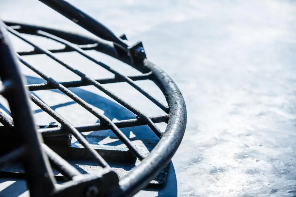 Nahaufnahme eines schwarzen Metallschutzgitters auf einem grauen Betonboden bei hellem Tageslicht