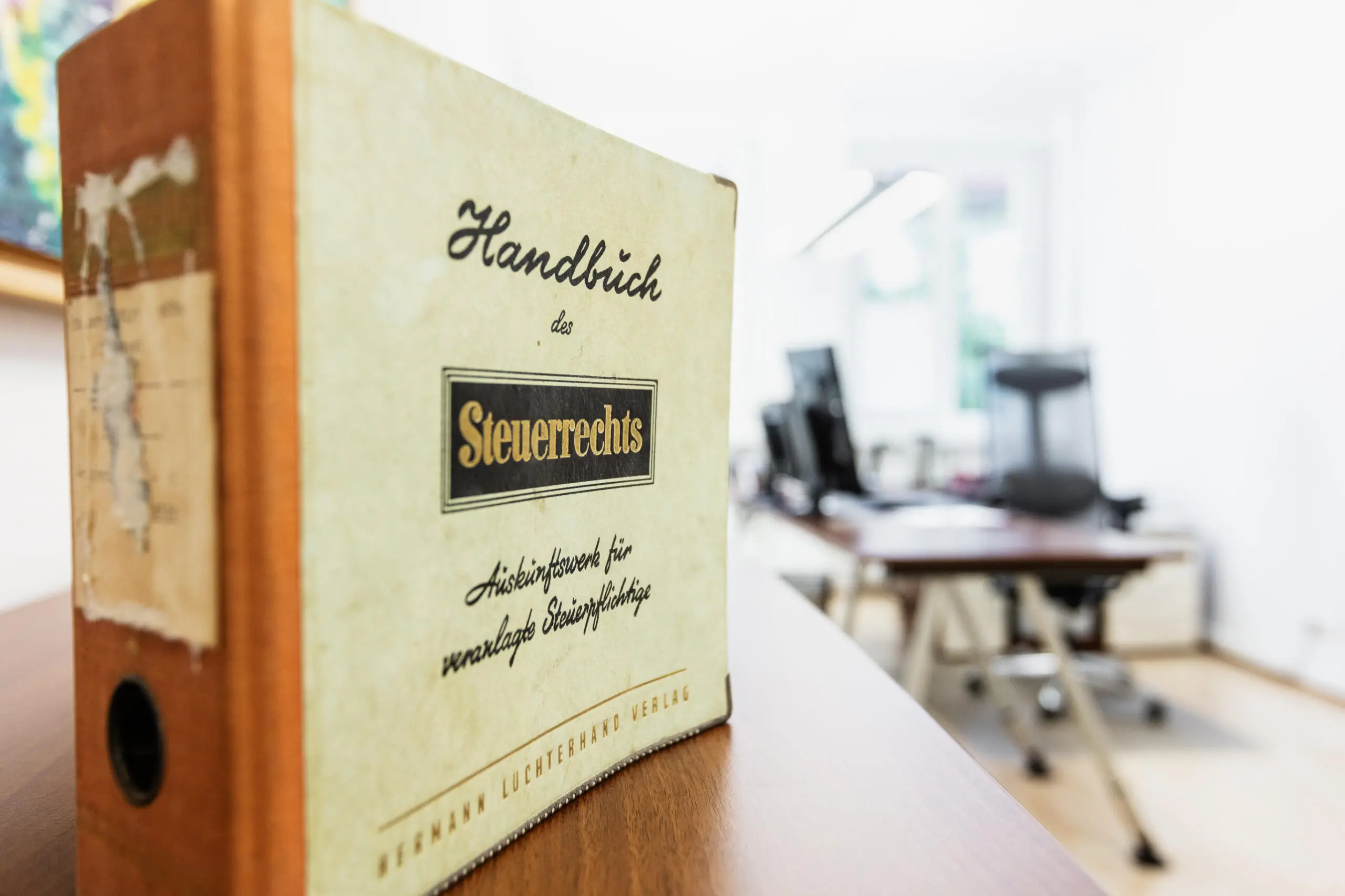 Nahaufnahme eines historischen Handbuchs des Steuerrechts auf einem Schreibtisch vor unscharfem Büro-Hintergrund.