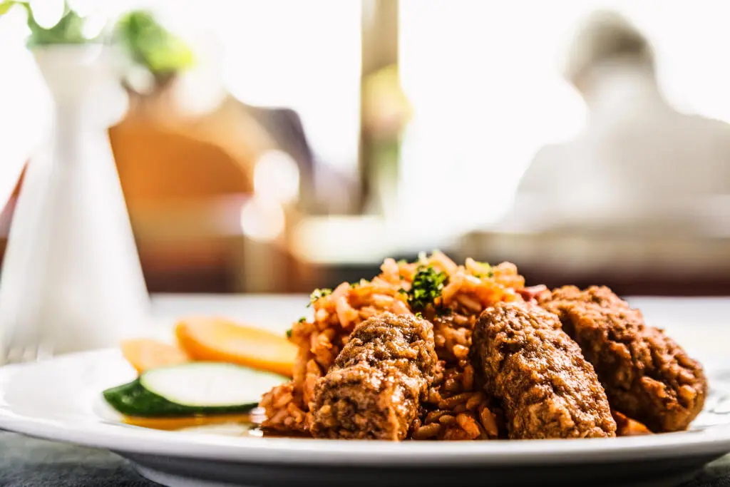 Teller mit Reis, Fleisch und Gemüse in hellen Tönen.