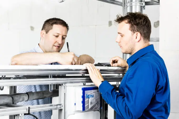 Zwei Handwerker in blauen Hemden besprechen Details an einem Installationsrahmen auf einer Baustelle