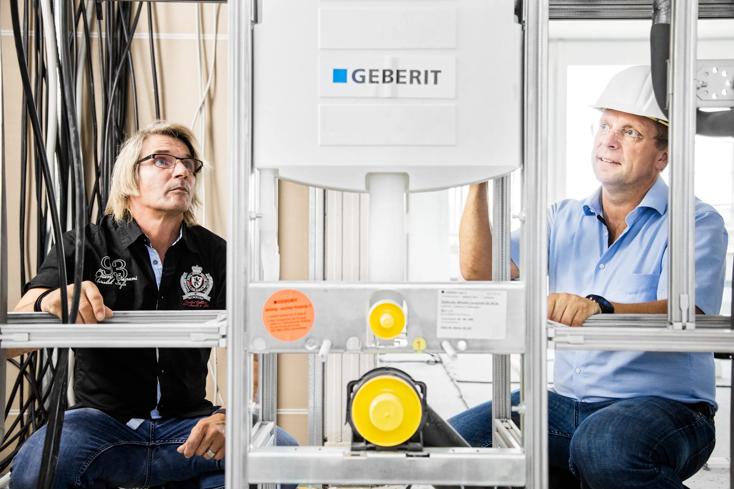 Zwei Handwerker bei der Begutachtung eines Sanitär-Installationsrahmens auf einer Baustelle