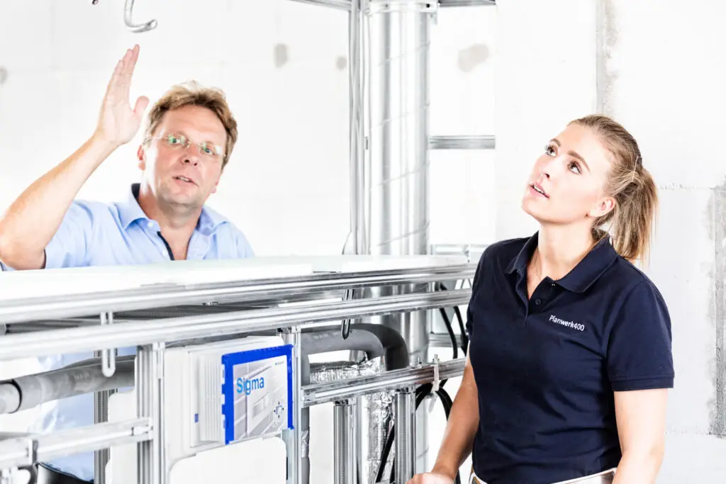 Mann und Frau bei der Begutachtung von Sanitärinstallationen und Rohrleitungen auf einer Rohbau-Baustelle