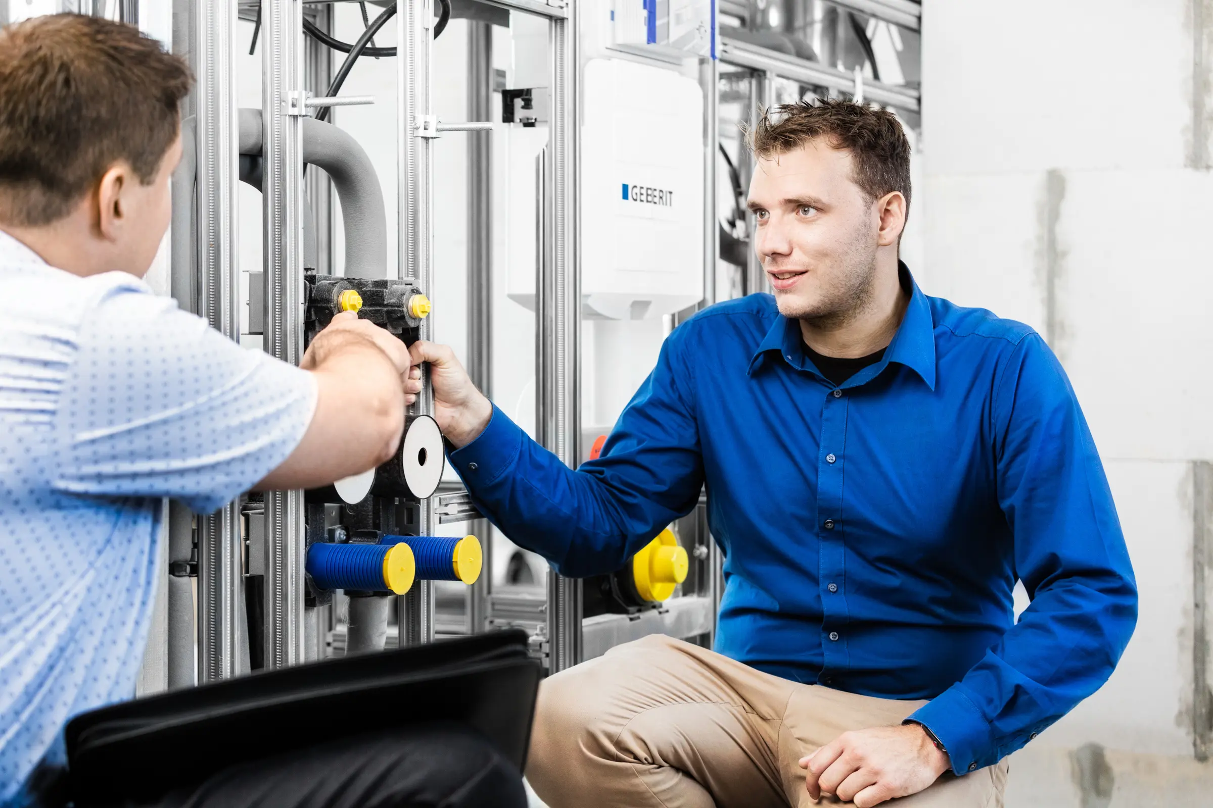 Zwei Männer im Gespräch vor einer Sanitär-Vorwandinstallation mit Rohren und Spülkasten auf einer Baustelle