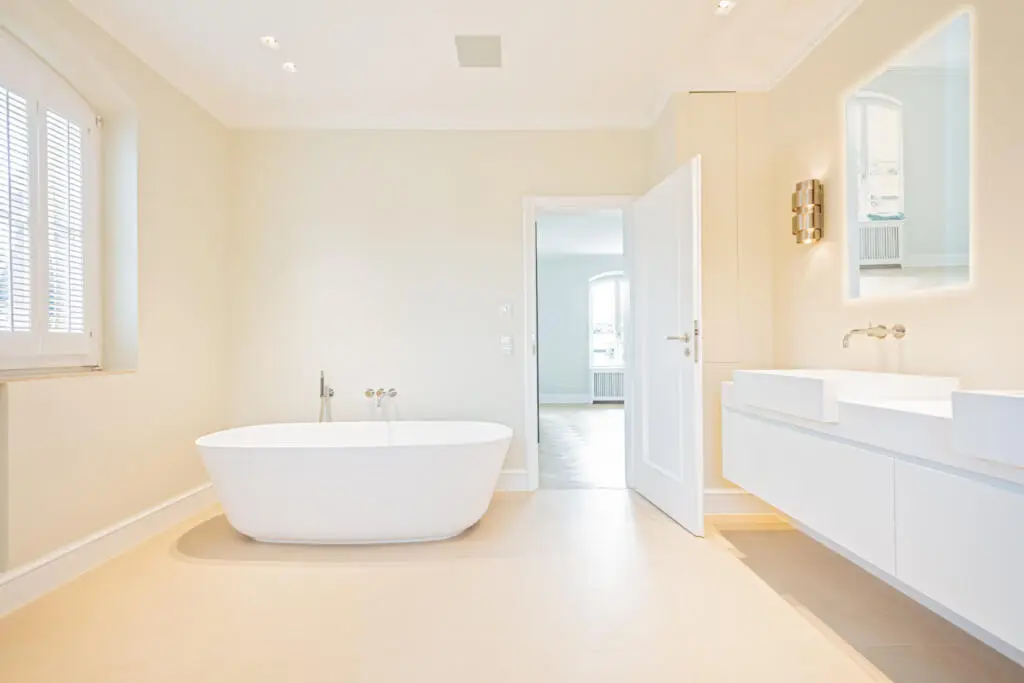 Helles Badezimmer mit freistehender weißer Badewanne, schwebendem Doppelwaschtisch und cremefarbenen Fliesen in einer modernen Villa.