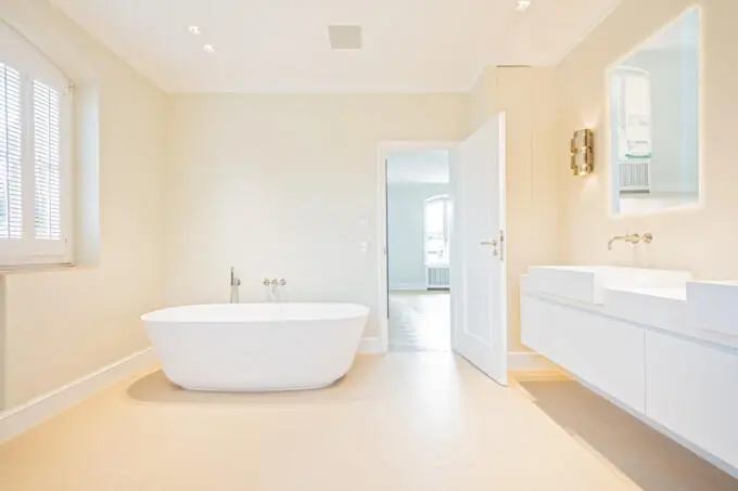 Helles Badezimmer mit freistehender weißer Badewanne, schwebendem Doppelwaschtisch und cremefarbenen Fliesen in einer modernen Villa.