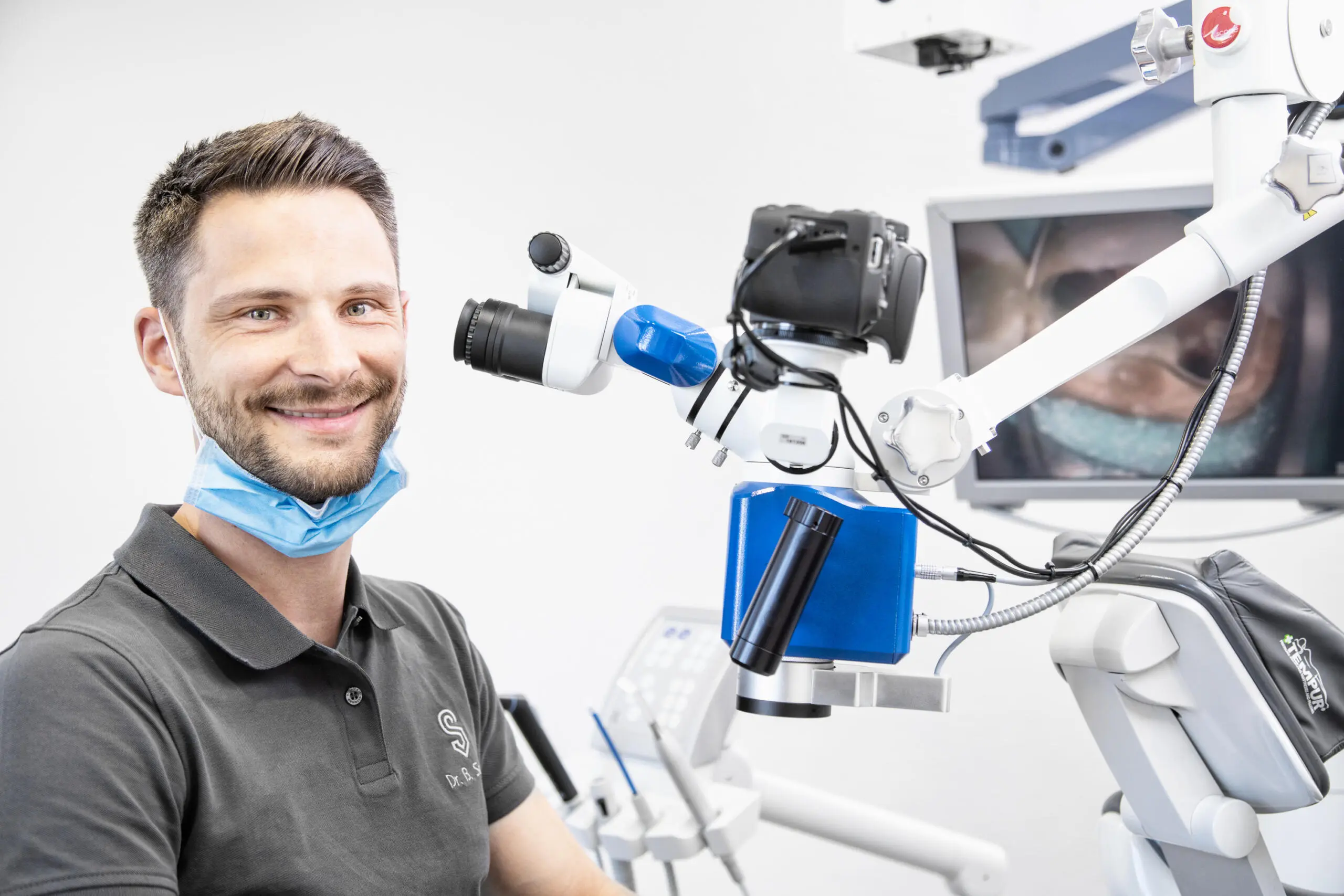 Zahnarzt lächelt neben hochmodernem Mikroskop.