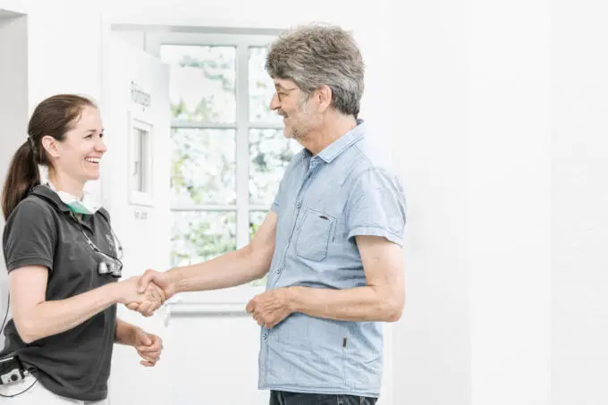 Zahnärztin begrüßt Patient mit Handschlag in heller Praxis.