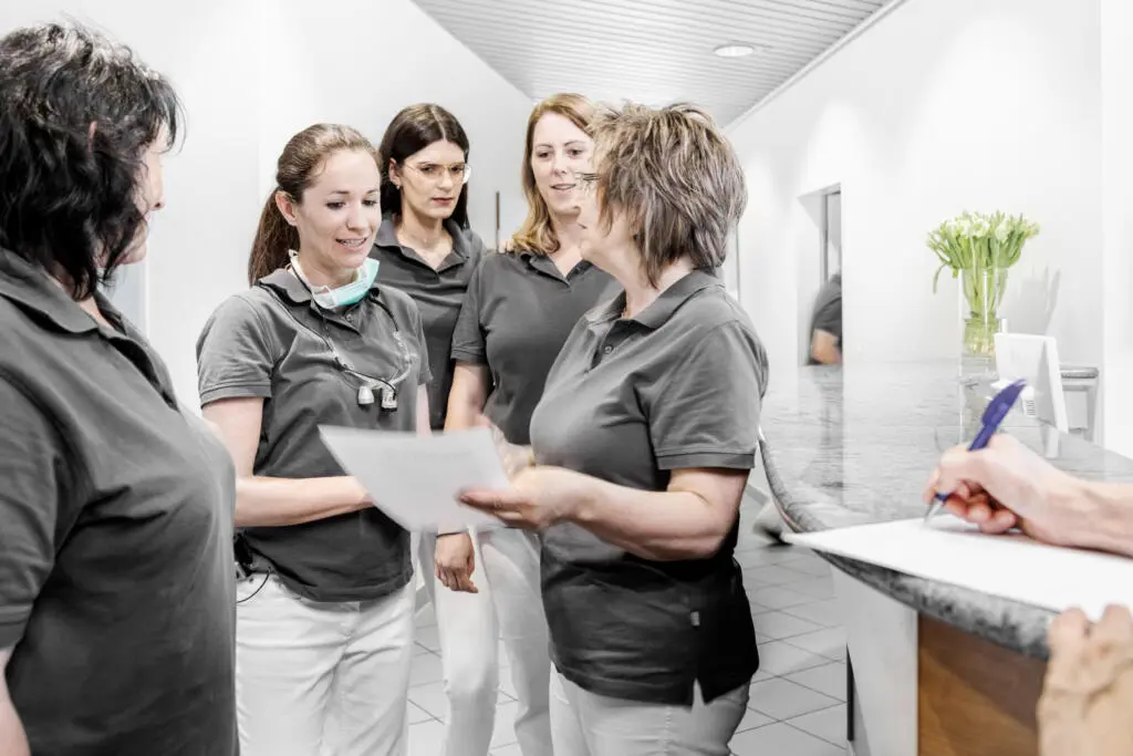 Zahnarztteam bespricht Patientenunterlagen in moderner Praxis.